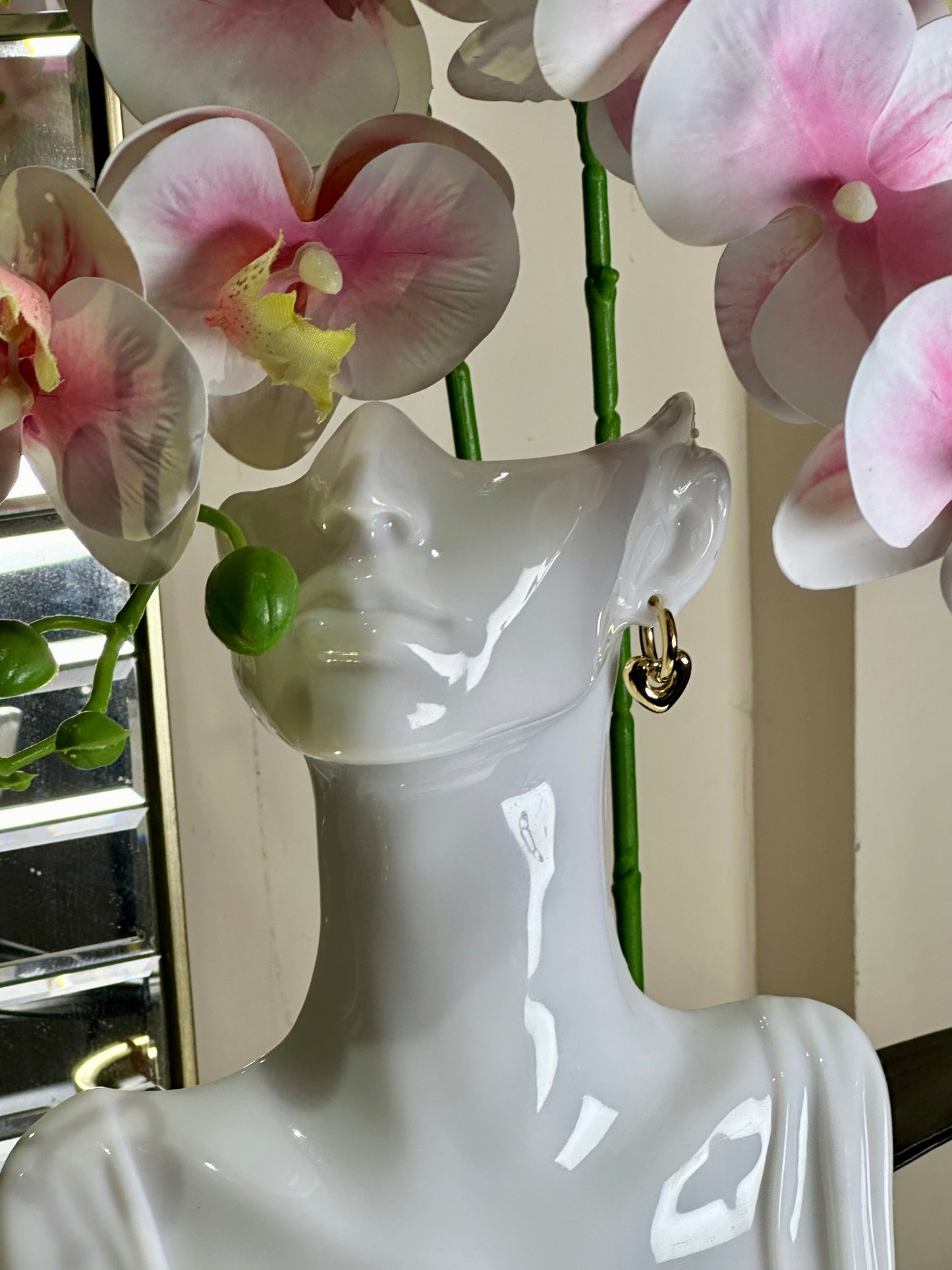 Heart Huggie Earring with stainless steel design on display mannequin, surrounded by pink flowers.
