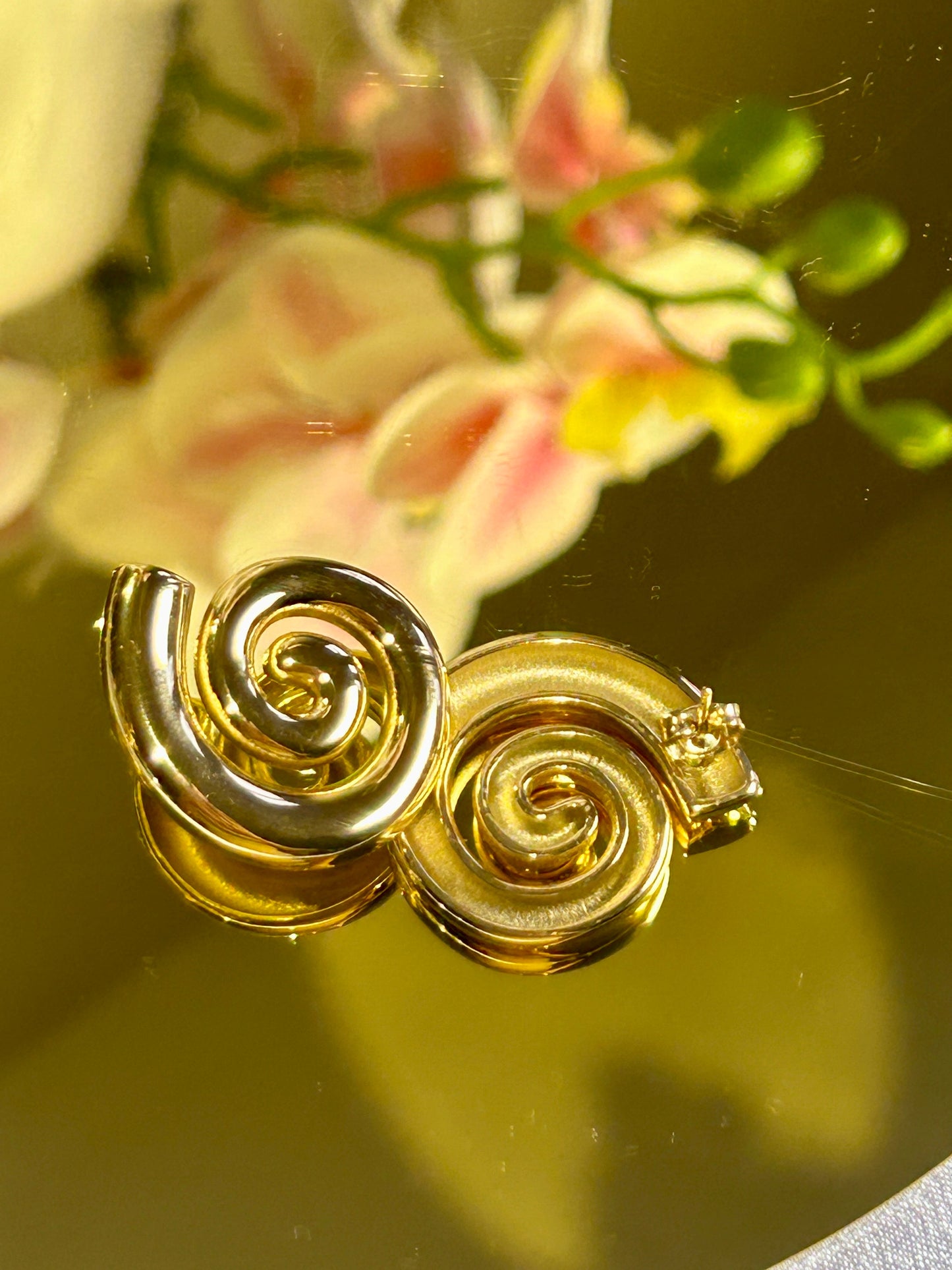 Geometric Spiral Stud Earrings in 18k gold plating on a reflective surface.