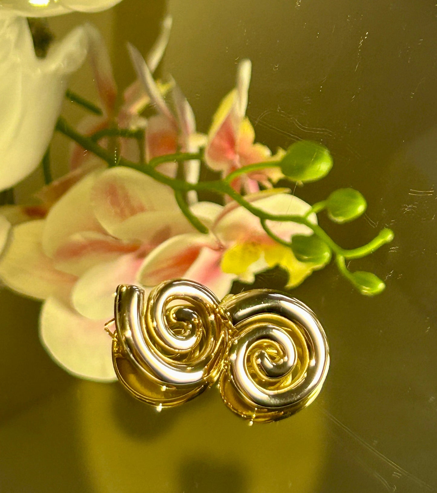 Geometric Spiral Stud Earrings with 18k gold plating on a floral background.