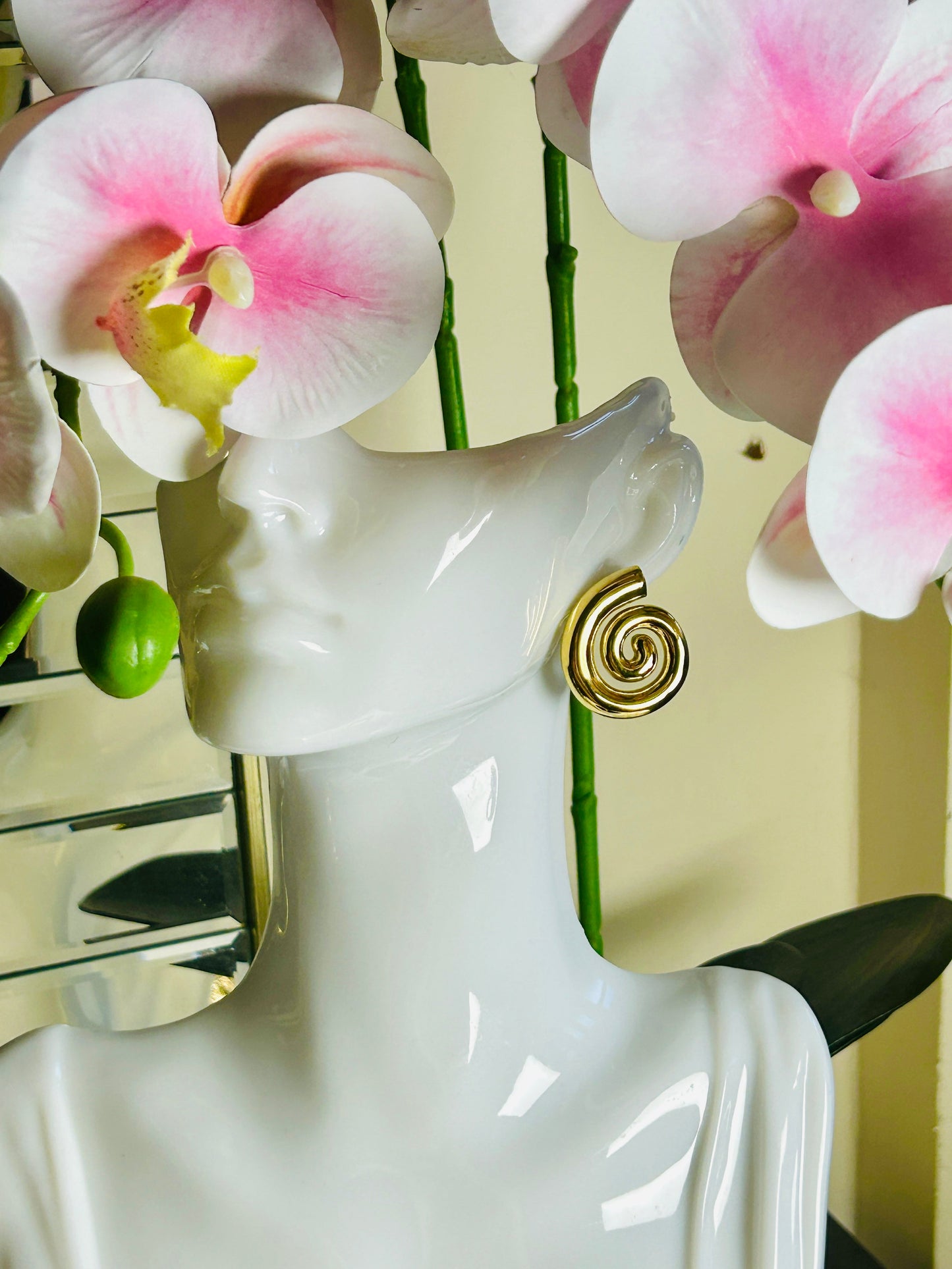 Geometric Spiral Stud Earrings in 18k gold plating on mannequin with pink flowers.