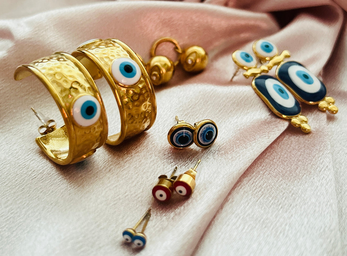 Devil Eye Earrings in stainless steel with 18k gold plating on a silk fabric background.