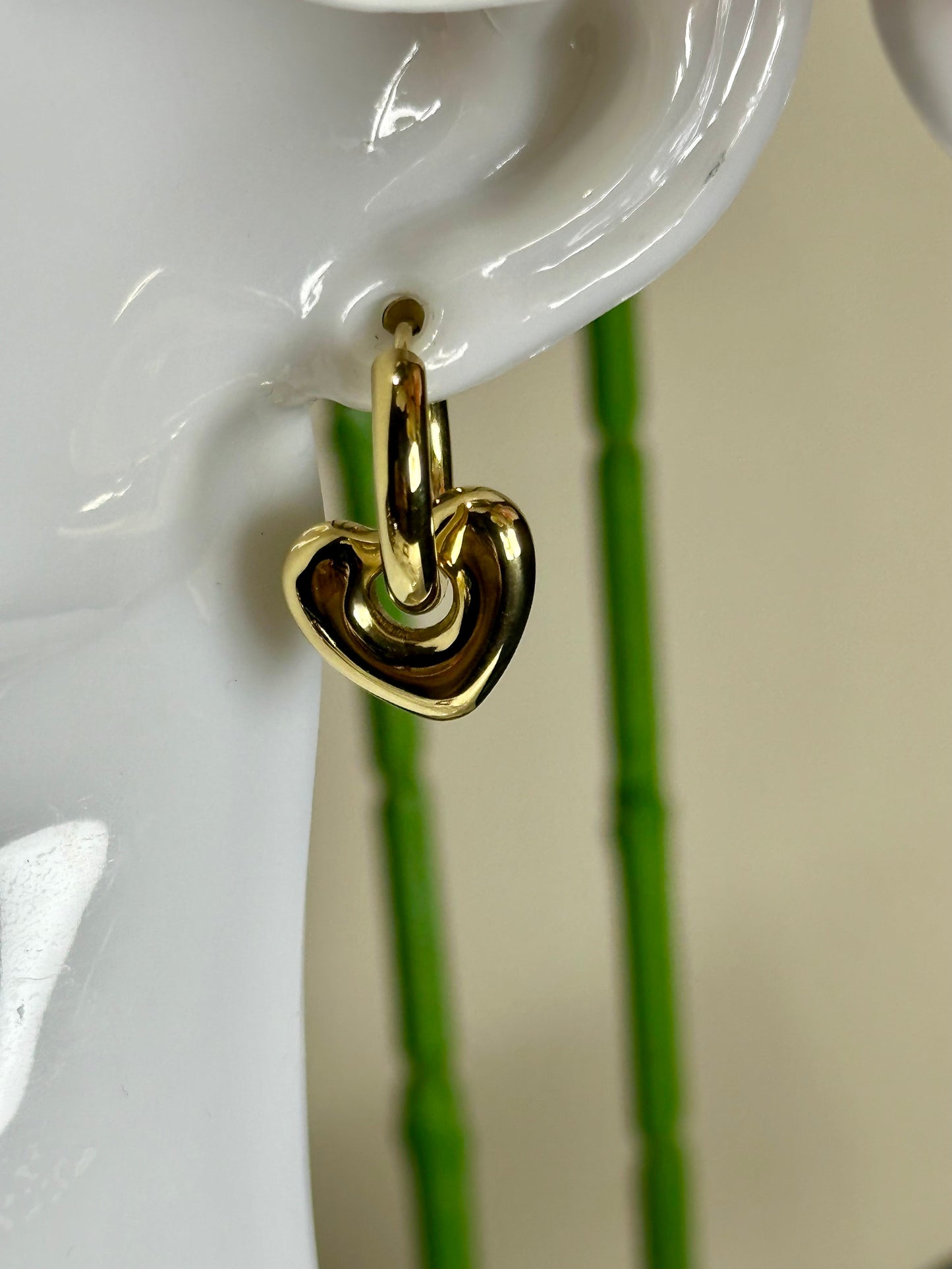 Heart Huggie Earring in stainless steel, heart-shaped design, shown on ear.