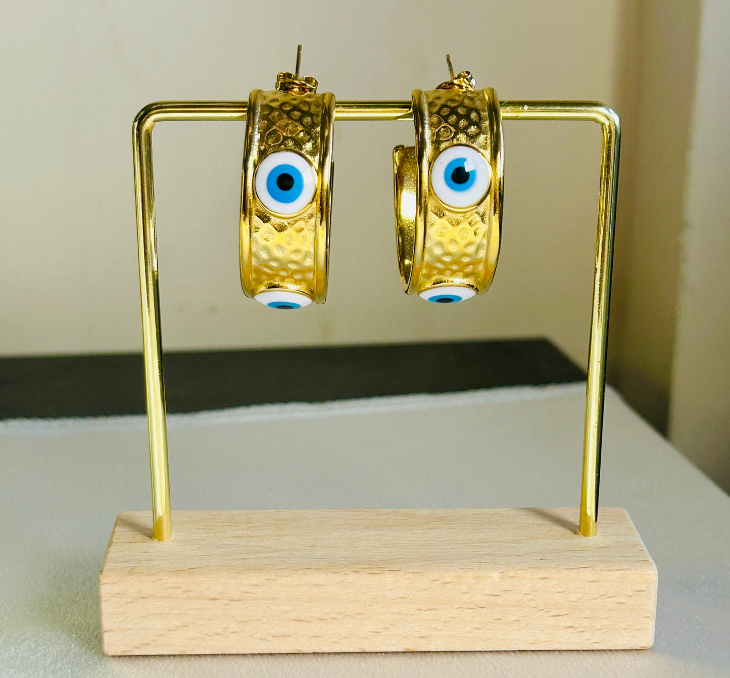 Devil Eye Earrings with 18k gold plating and stainless steel on a display stand.