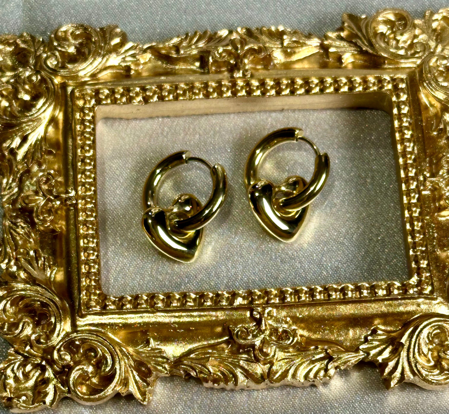 Heart Huggie Earrings in gold-tone stainless steel displayed in ornate frame.