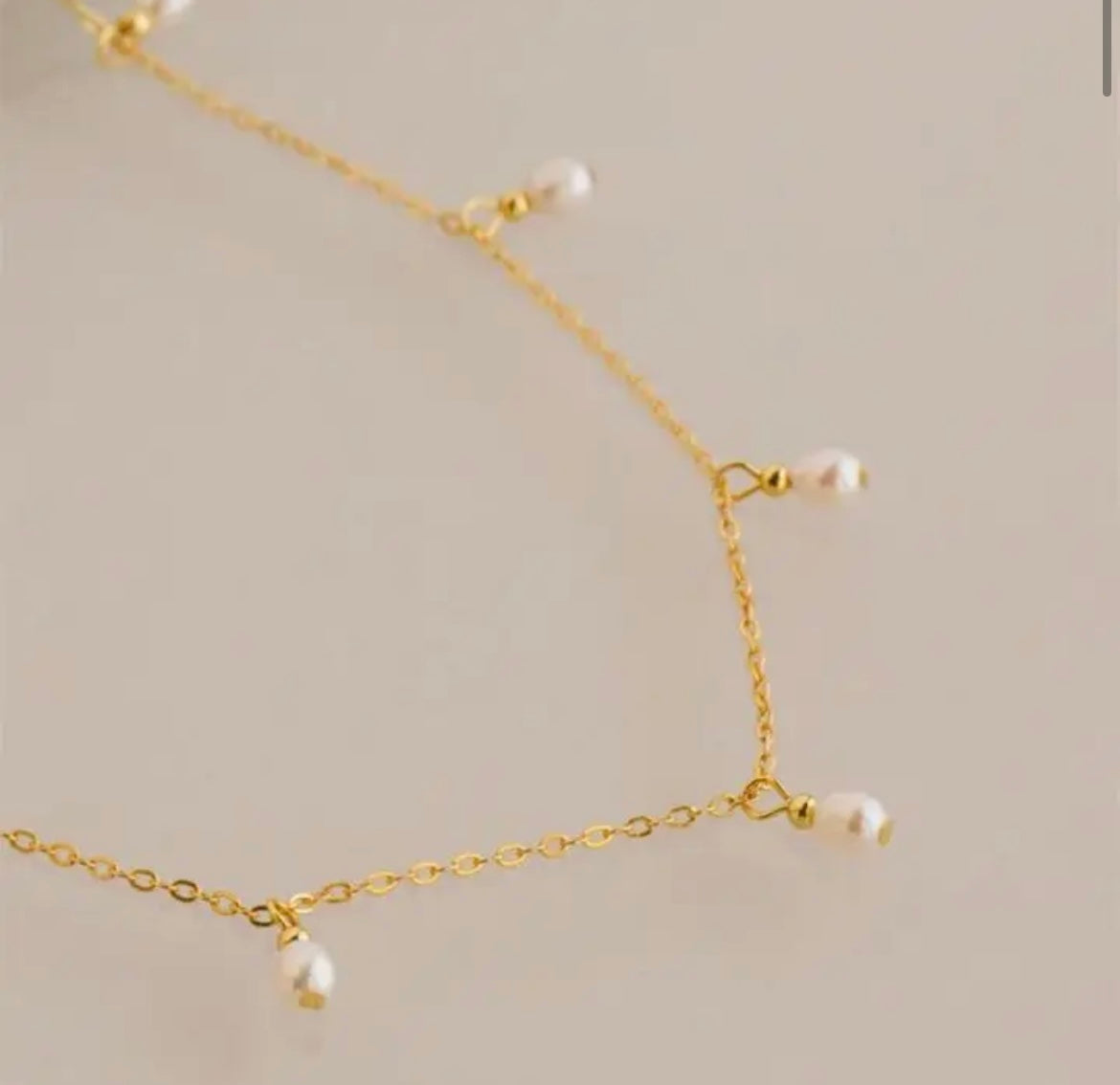 Gold-plated stainless steel teardrop imitation pearl necklace on display.