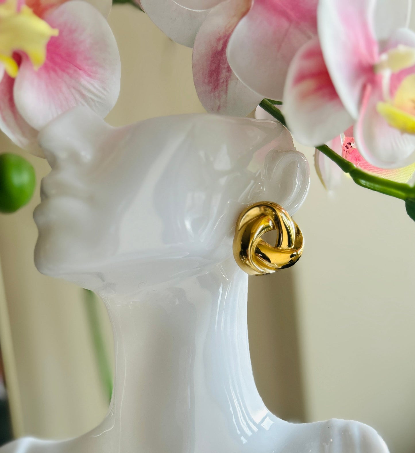 Vintage braided stud earring in gold, displayed on a mannequin near pink orchids.